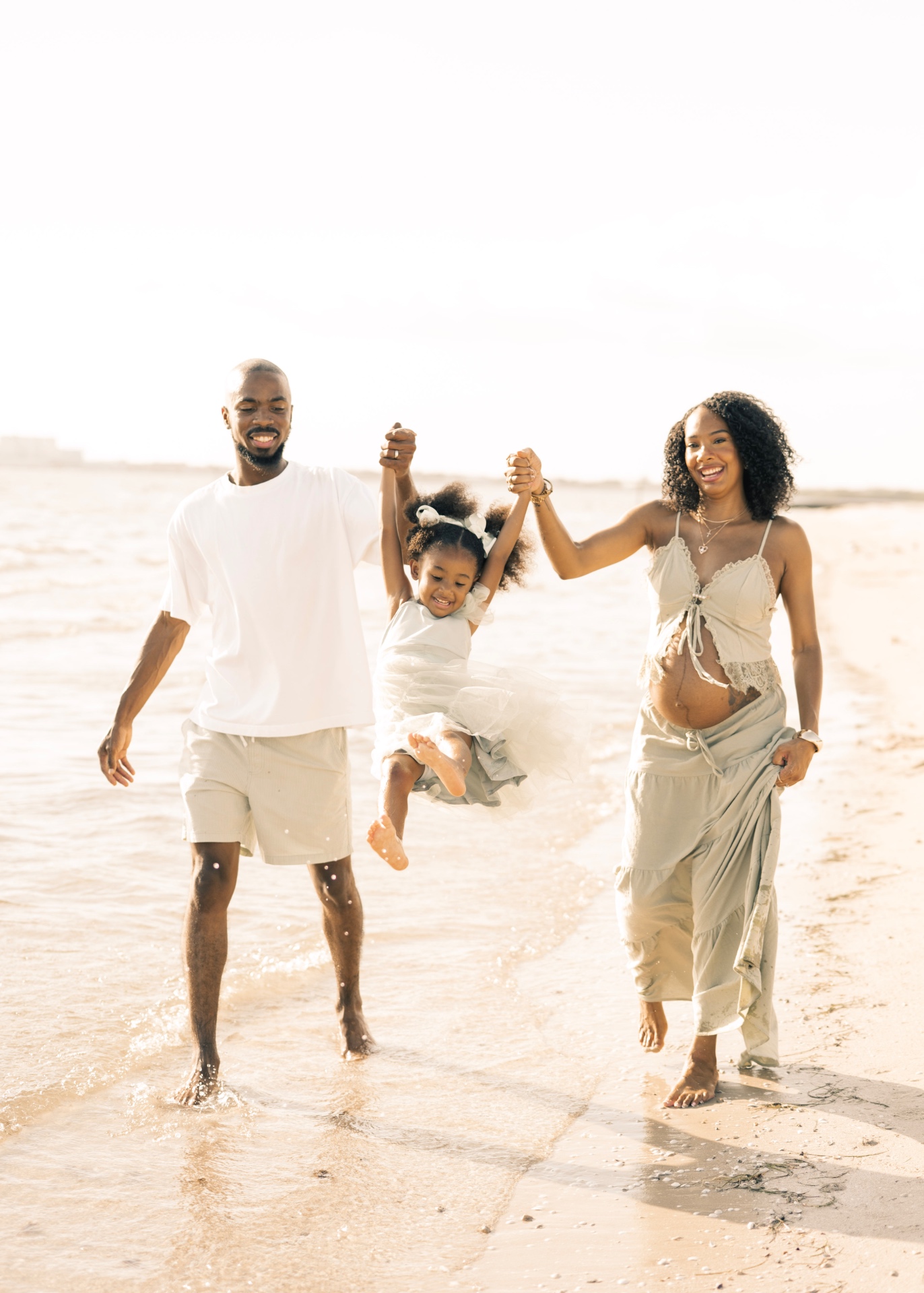 Family walking through shallow surf, expecting mother smiling