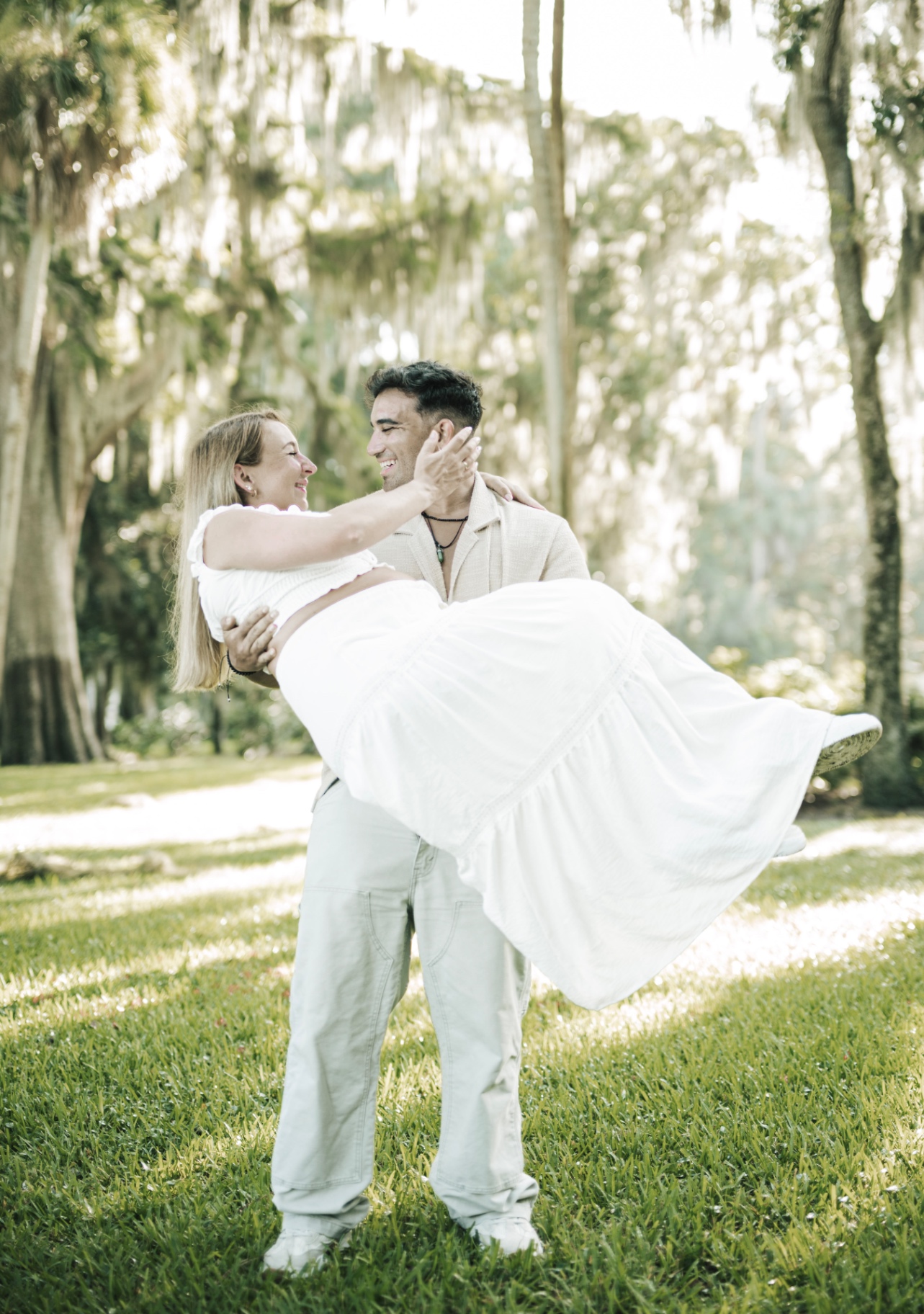 Groom carrying his bride beneath moss-draped oaks