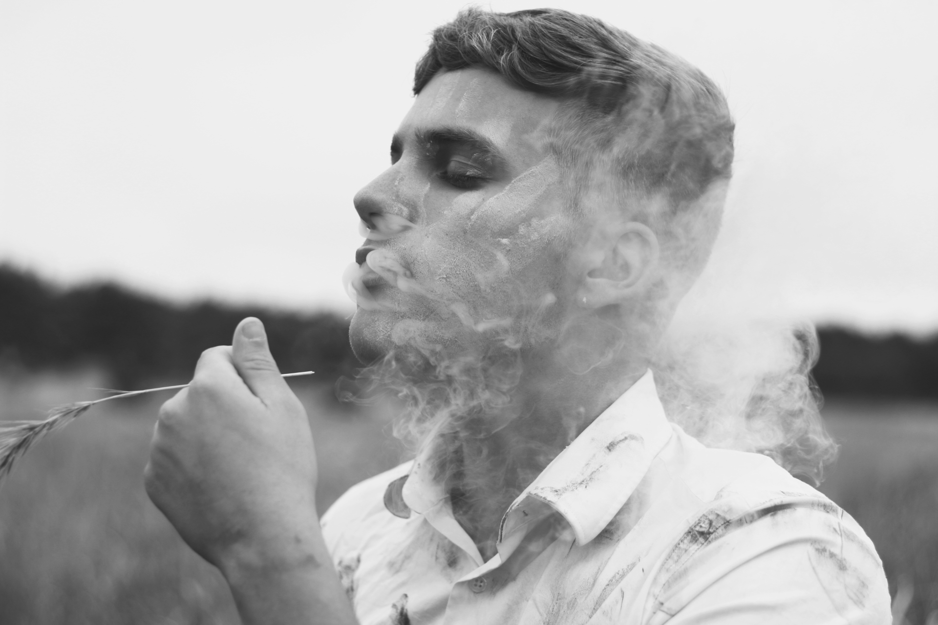 Black-and-white portrait of a man exhaling smoke in a field