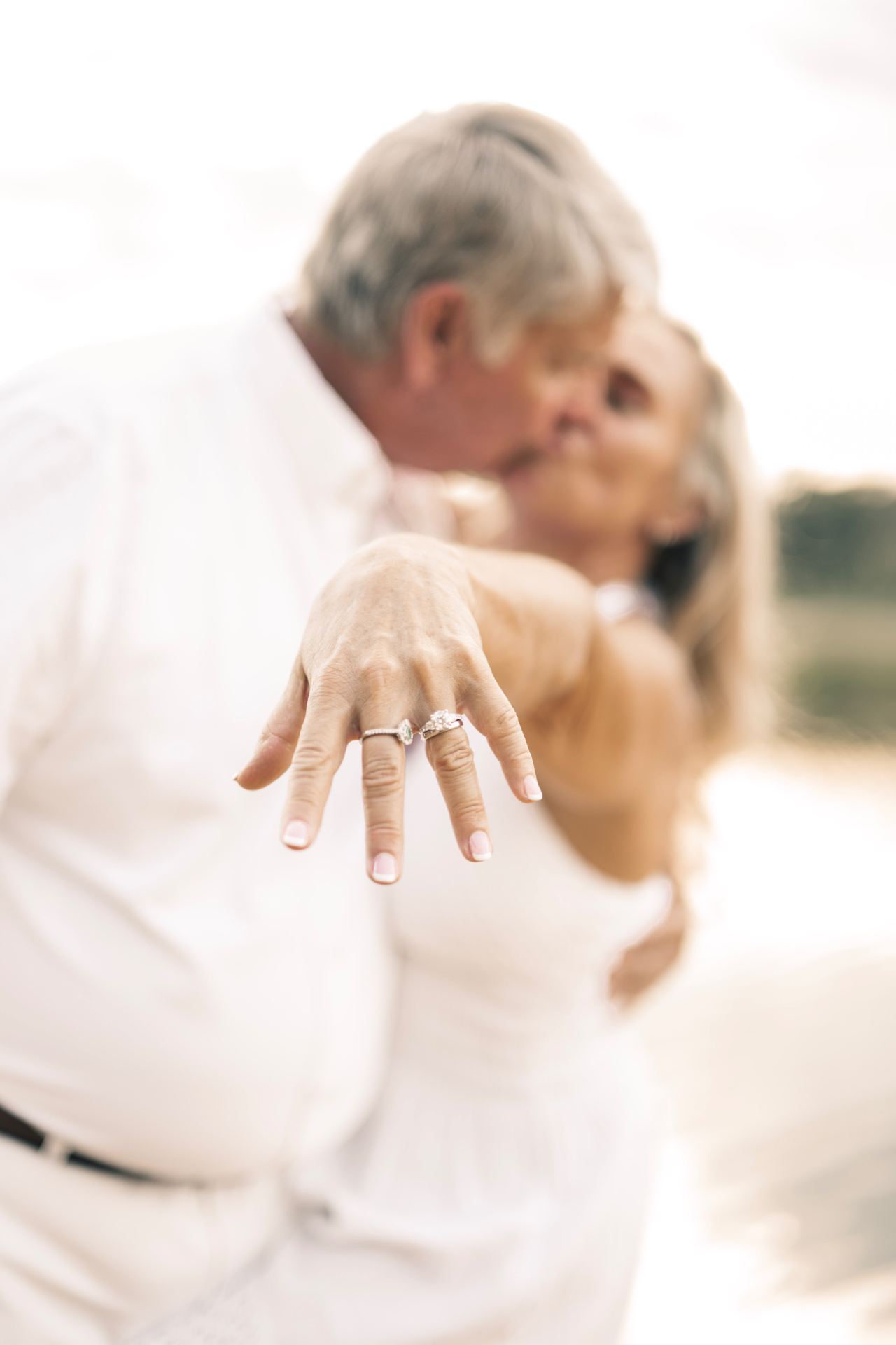 Couple sharing a kiss, wedding rings extended toward the camera
