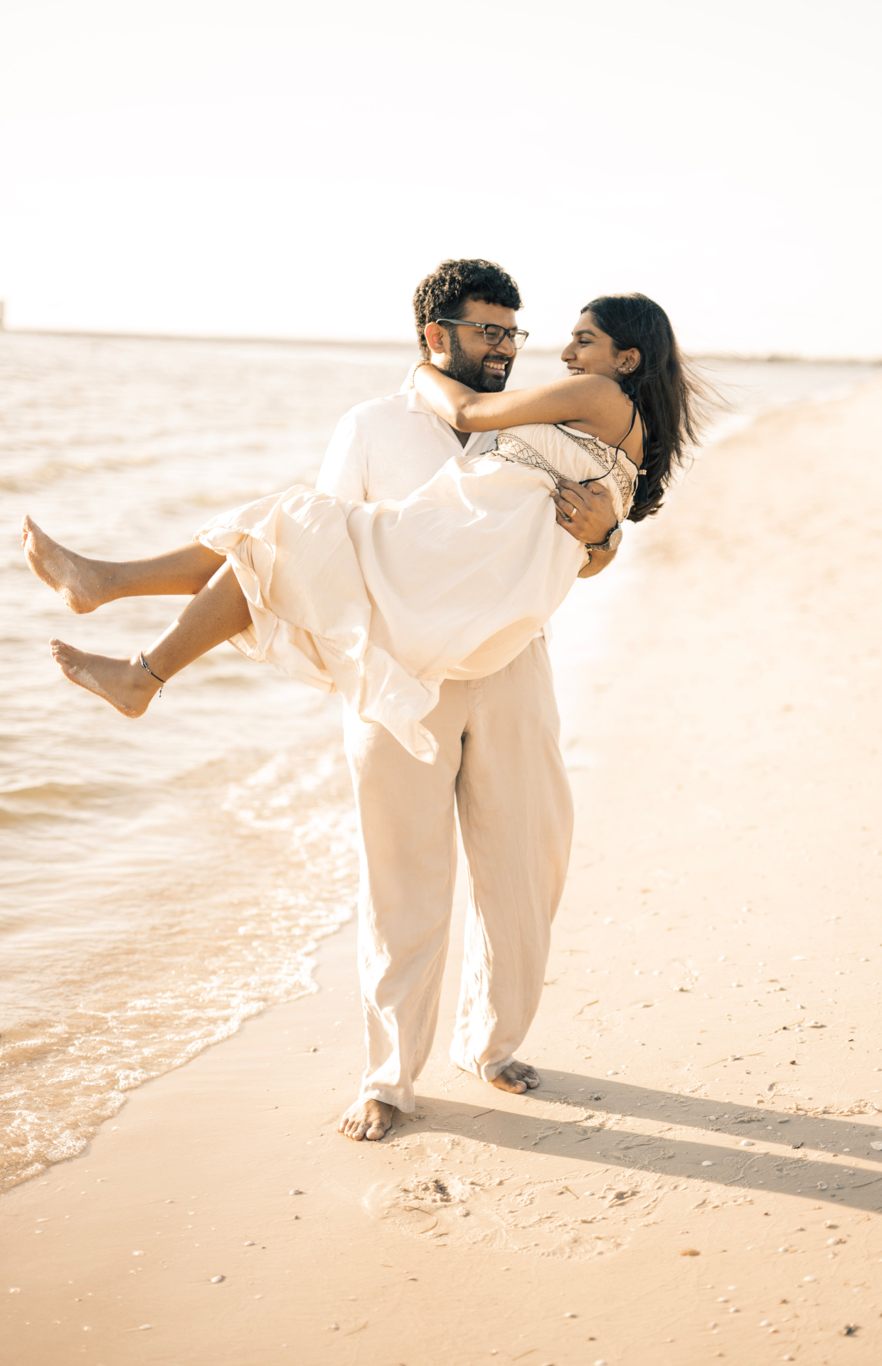 Groom carrying his bride along a sunlit shoreline